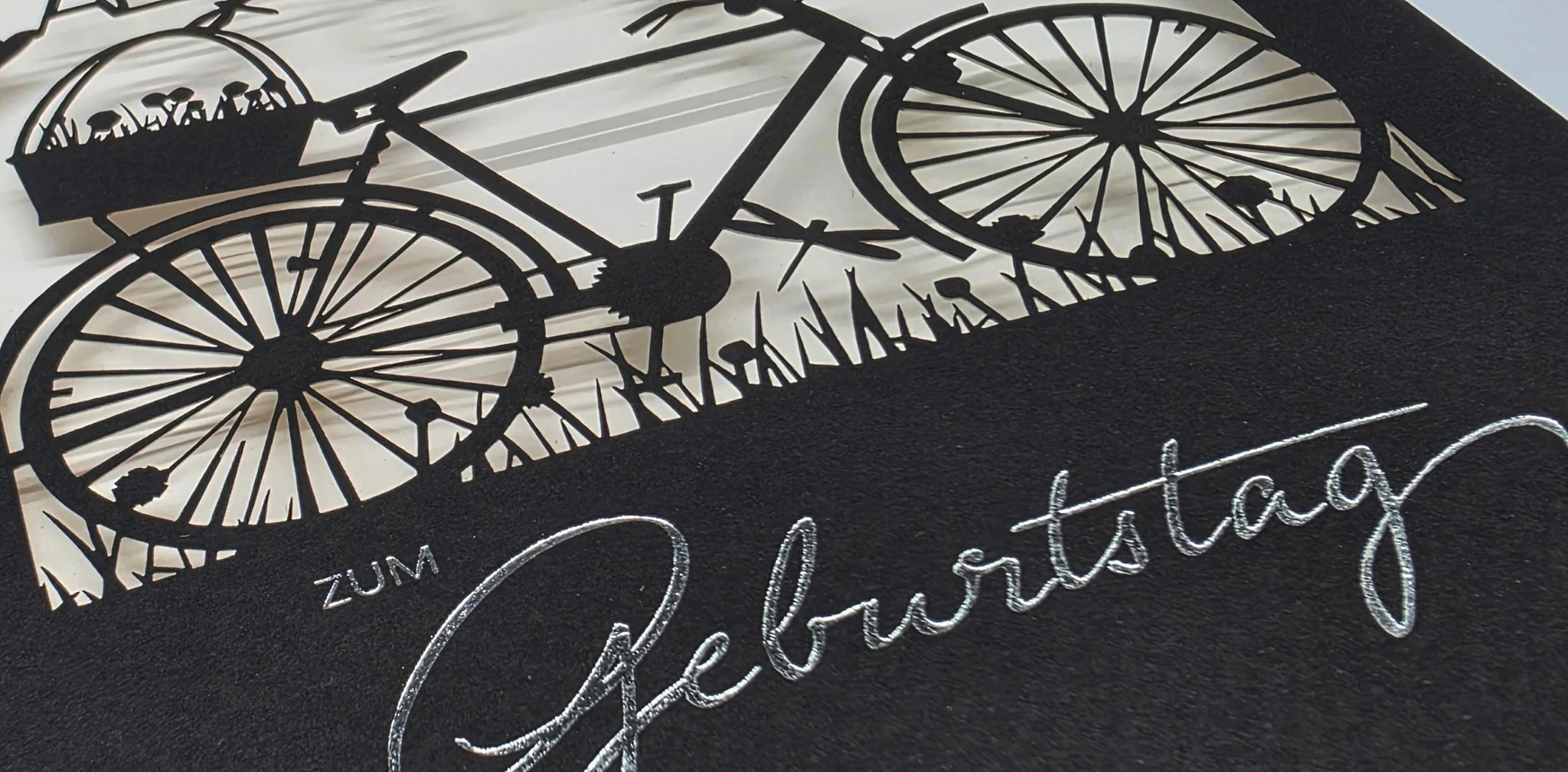 Filigraner Lasercut auf dunkelblauem Papier mit feiner Schrift und Fahrradmotiv